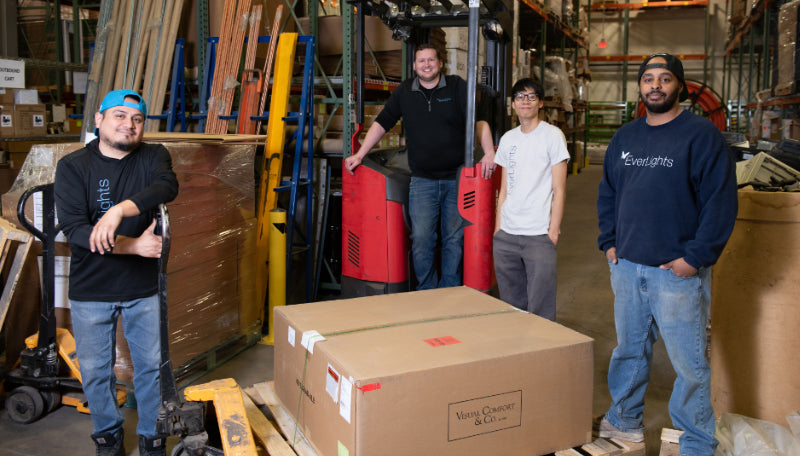 Four individuals standing in a warehouse with boxes and equipment.